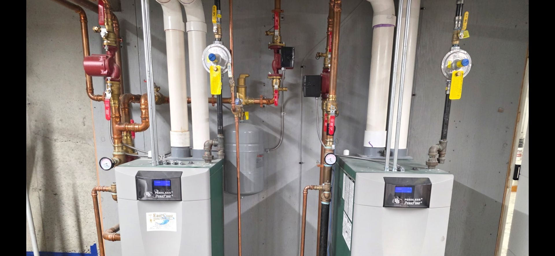 Two white boiler units with copper pipes and valves in a utility room