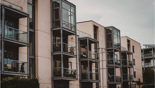 A row of modern, beige apartment buildings featuring protruding, glass-enclosed balcony structures.