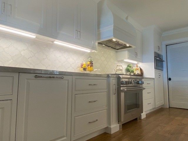 Bright white modern kitchen with cabinets, stainless stove, and wood floors