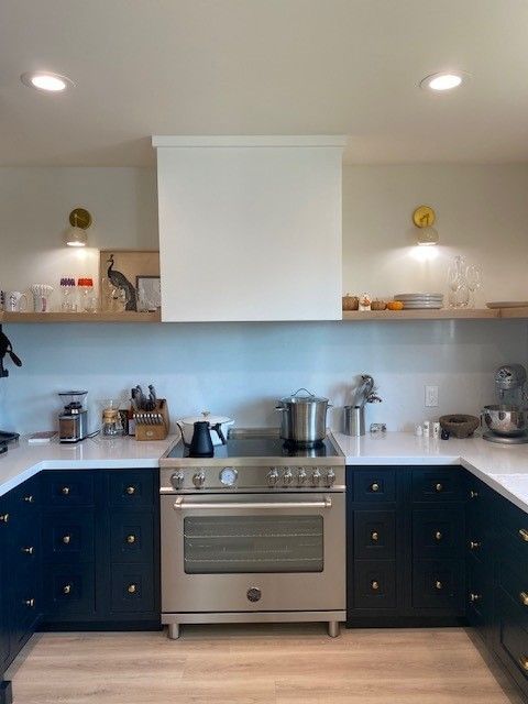 Modern kitchen with navy cabinets, stainless steel stove, white shelves, and a large central range hood