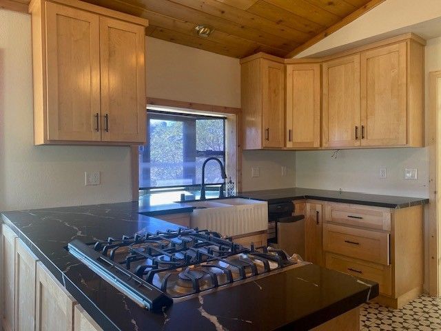 Small kitchen with wood cabinets, black countertop, gas stove, and sink under a window