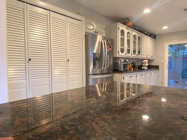 Bright kitchen with white cabinets, stainless fridge, and dark granite island countertop