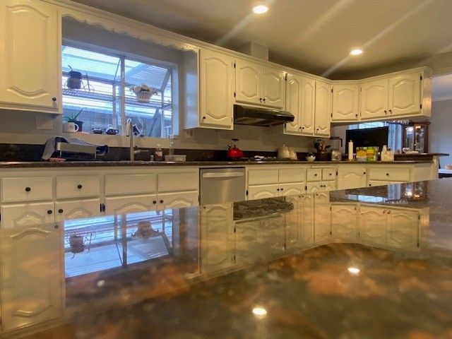 Bright kitchen with white cabinets, window over sink, and a glossy marble island reflecting the room.
