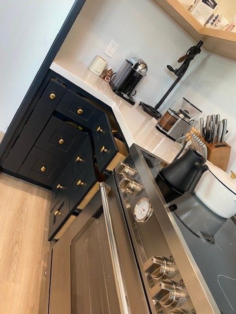 Tilted view of a modern kitchen with dark cabinets, white counters, and a stainless steel oven and kettle.