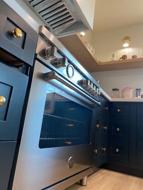 Stainless steel oven in a dark blue kitchen with cabinets and a range hood overhead
