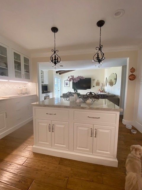 Bright white kitchen island with pendant lights, wood floor, and open view to a living room.