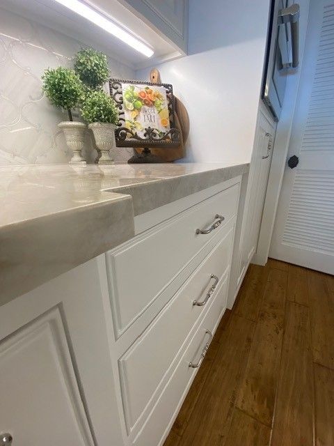 White hallway cabinet with marble top, potted plant, framed photo, and wooden floor in a narrow entryway