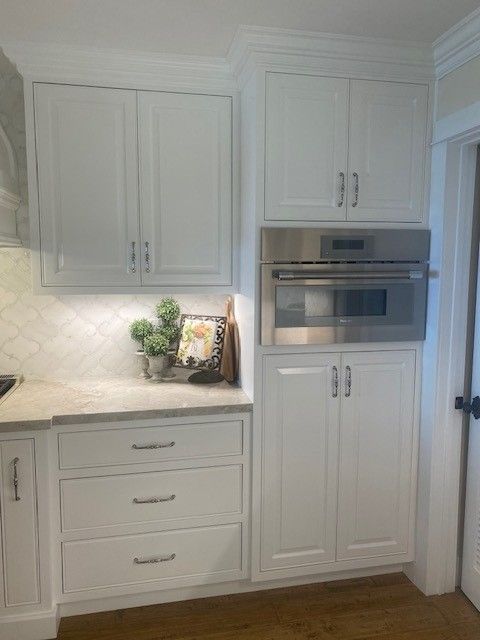 White kitchen cabinets with built-in oven, marble backsplash, and light countertop decor