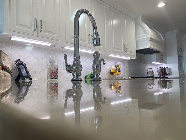 Modern kitchen with glossy countertops, white cabinets, and a chrome faucet in the center.