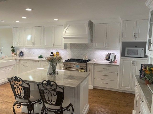 Bright white kitchen with island, bar stools, and stainless appliances on wood floor