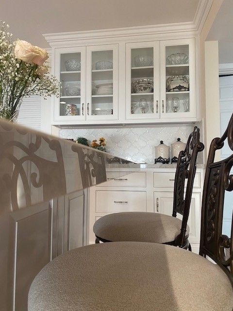 Elegant dining room with beige chairs, white cabinets, and glass-front display shelves