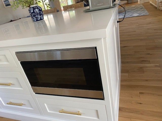White kitchen island with built-in stainless steel oven and drawers on a hardwood floor.