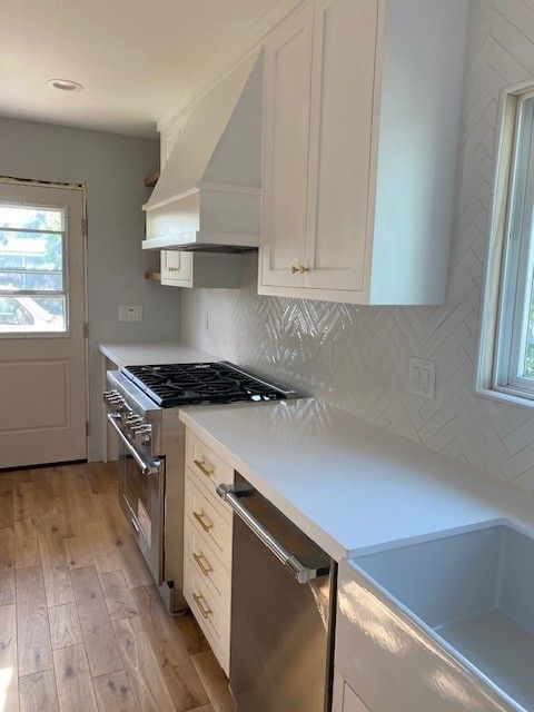 Narrow galley kitchen with white cabinets, stainless appliances, and a light wood floor.