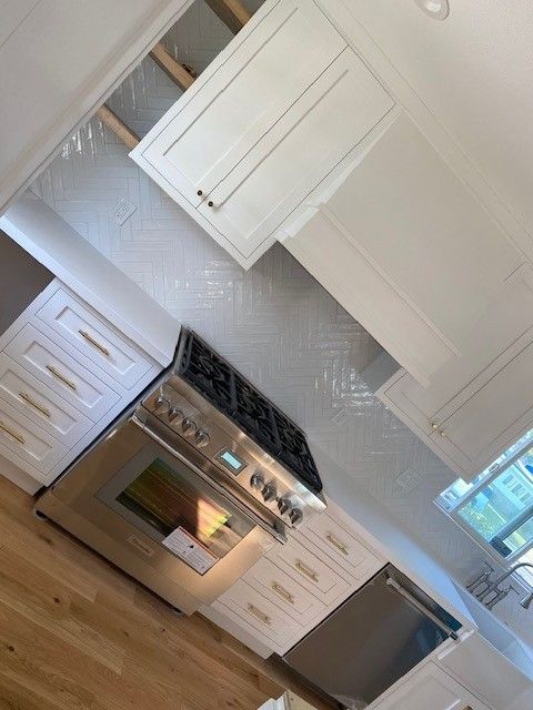 Bright kitchen with white cabinets, gas stove, wood floors, and a stainless steel dishwasher.