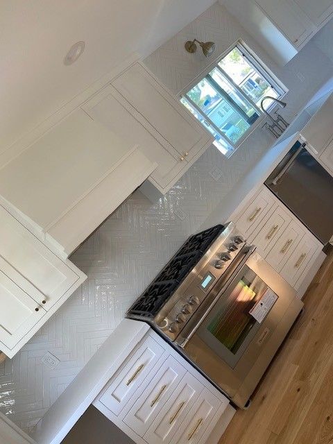 Bright white kitchen with stainless steel stove, wood floor, and window by the sink.