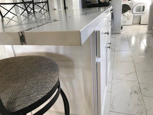 White kitchen island with marble floor, round stool, and folding chair by a bright window