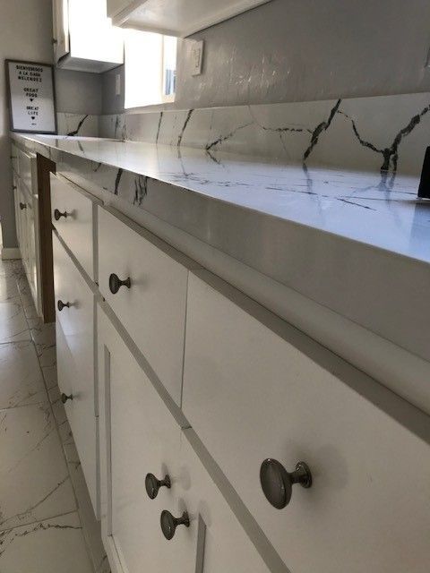White bathroom vanity with marble countertop, drawers, and cabinets along a tiled floor