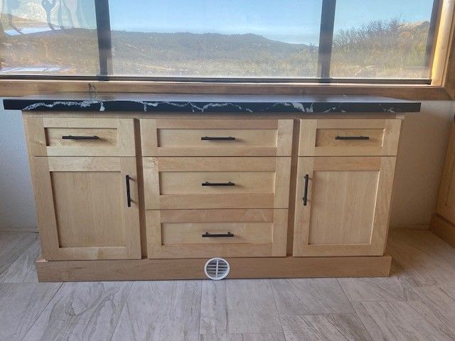 Light wood kitchen cabinet with black countertop beneath a window and mountains outside