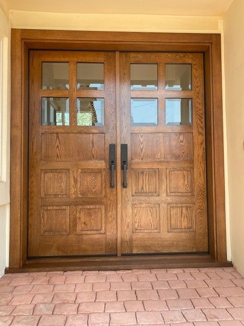 Wooden double front doors with glass panes above a pink brick walkway