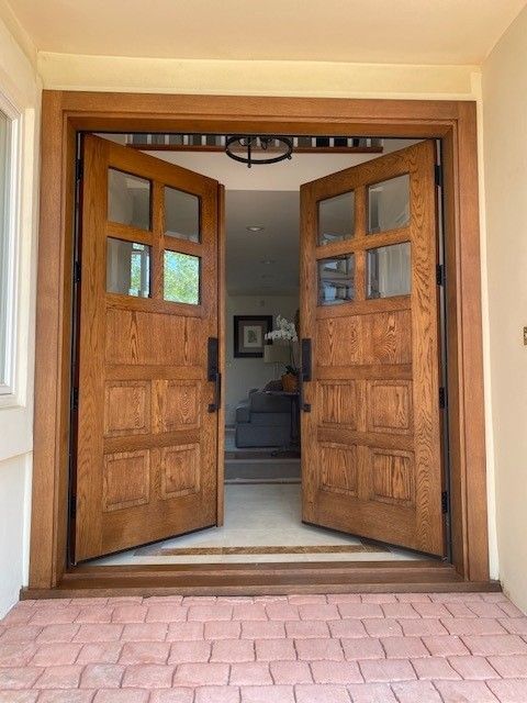 Wooden double front doors open onto a tiled entryway leading into a home.