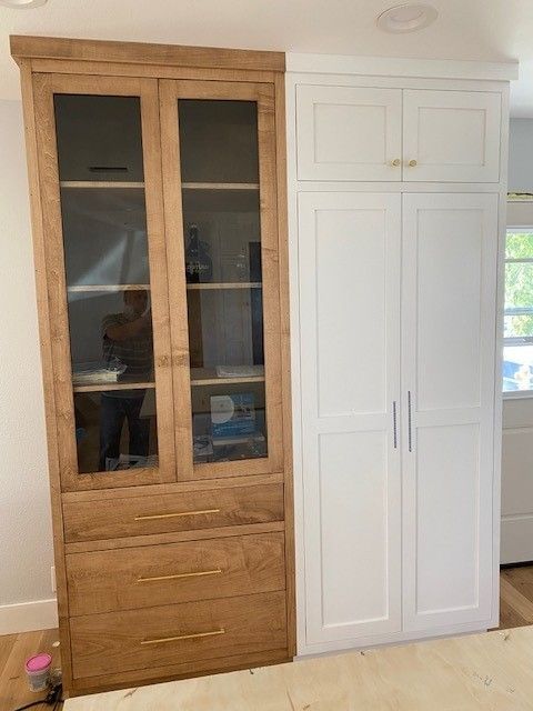 Wooden display cabinet beside a white wardrobe in a bright room