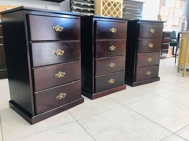 Three dark wood chests of drawers with brass handles lined up on a tiled floor in a room
