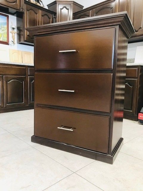 Dark wood three-drawer dresser with silver handles in a furniture showroom