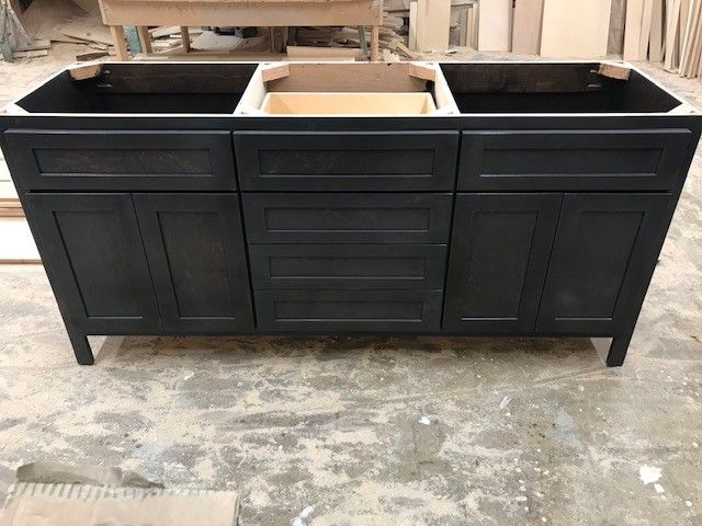 Black three-basin vanity cabinet with white sink basins in a workshop setting