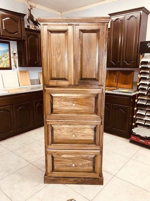 Tall wooden cabinet with paneled doors and drawers in a kitchen showroom