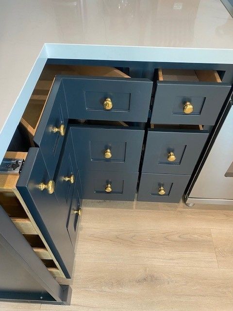 Open navy kitchen cabinet with brass knobs and drawers, partially pulled out beside a stainless appliance.