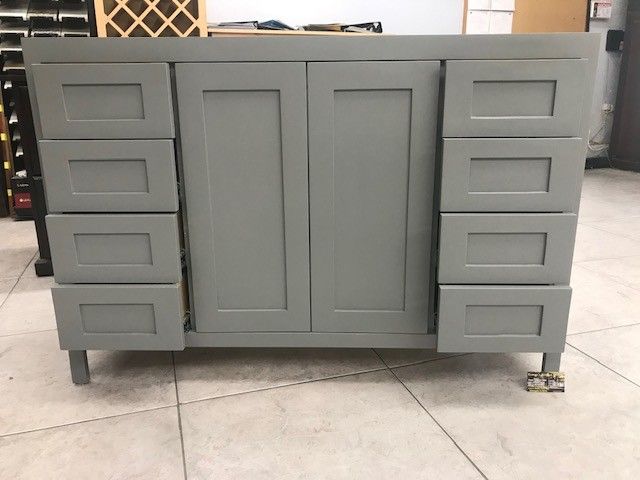 Gray bathroom vanity cabinet with six drawers and double center doors, standing on a tiled floor.