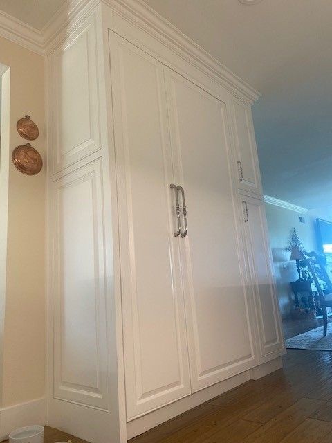 White built-in closet cabinets in a hallway with hardwood floor and crown molding