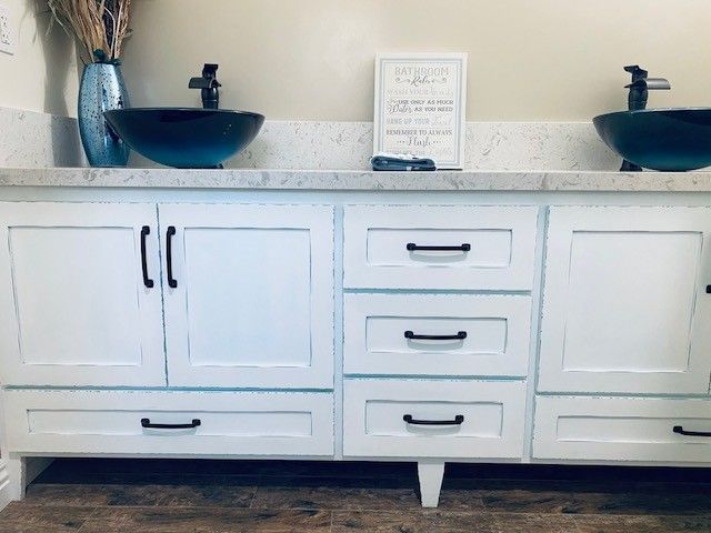 White bathroom vanity with blue vessel sinks, three central drawers, and countertop decor