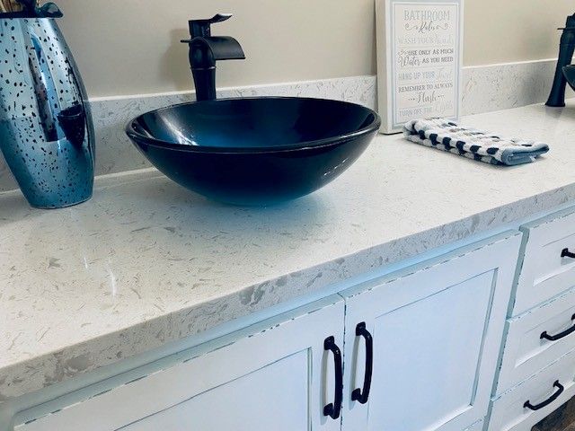 Bathroom vanity with a black vessel sink, blue glass vase, soap dispenser, and decorative tray on a white countertop