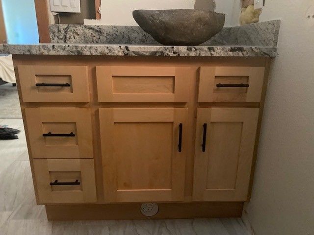 Bathroom vanity with light wood cabinets, granite countertop, and a stone bowl sink