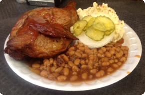 Plate of barbecue with chicken, baked beans, potato salad, pickles, and onion.