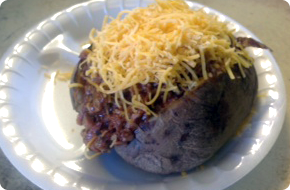 Baked potato, stuffed with meat and topped with shredded cheese, on a white plate.