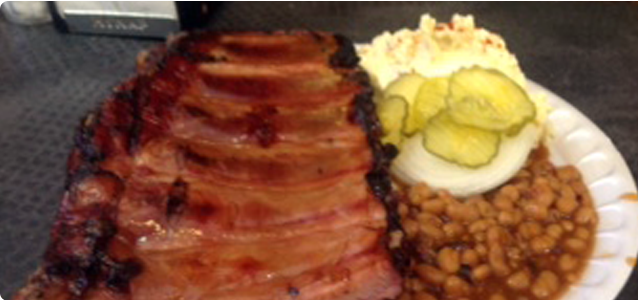 Rack of ribs with sides of baked beans, pickles, and mashed potatoes.