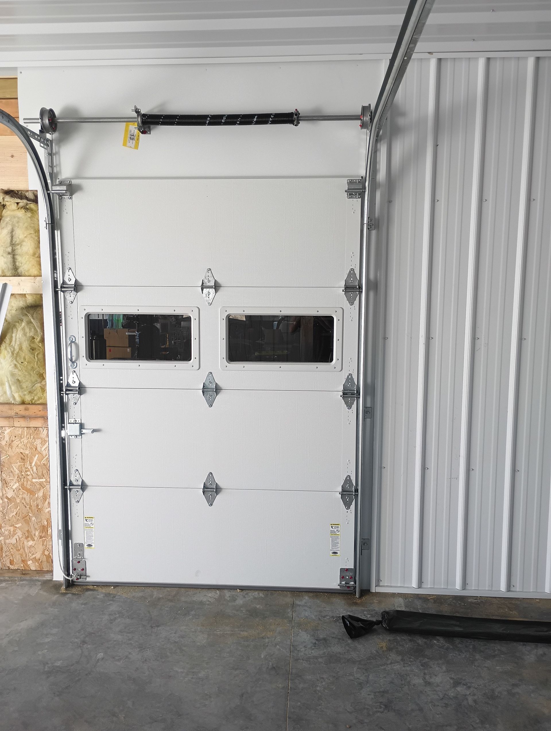 White garage door with windows, metal track, and corrugated wall panels.