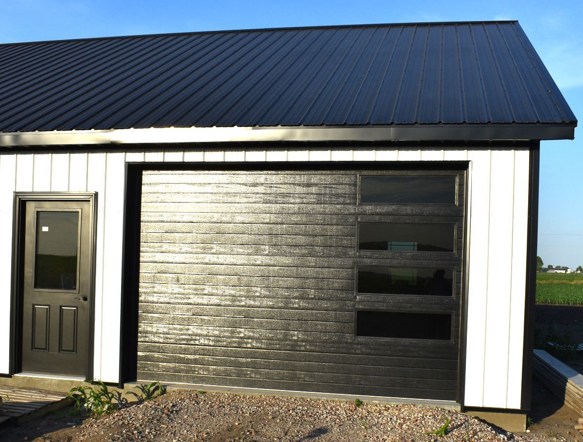 Black garage door with windows and a black roof on a white building.