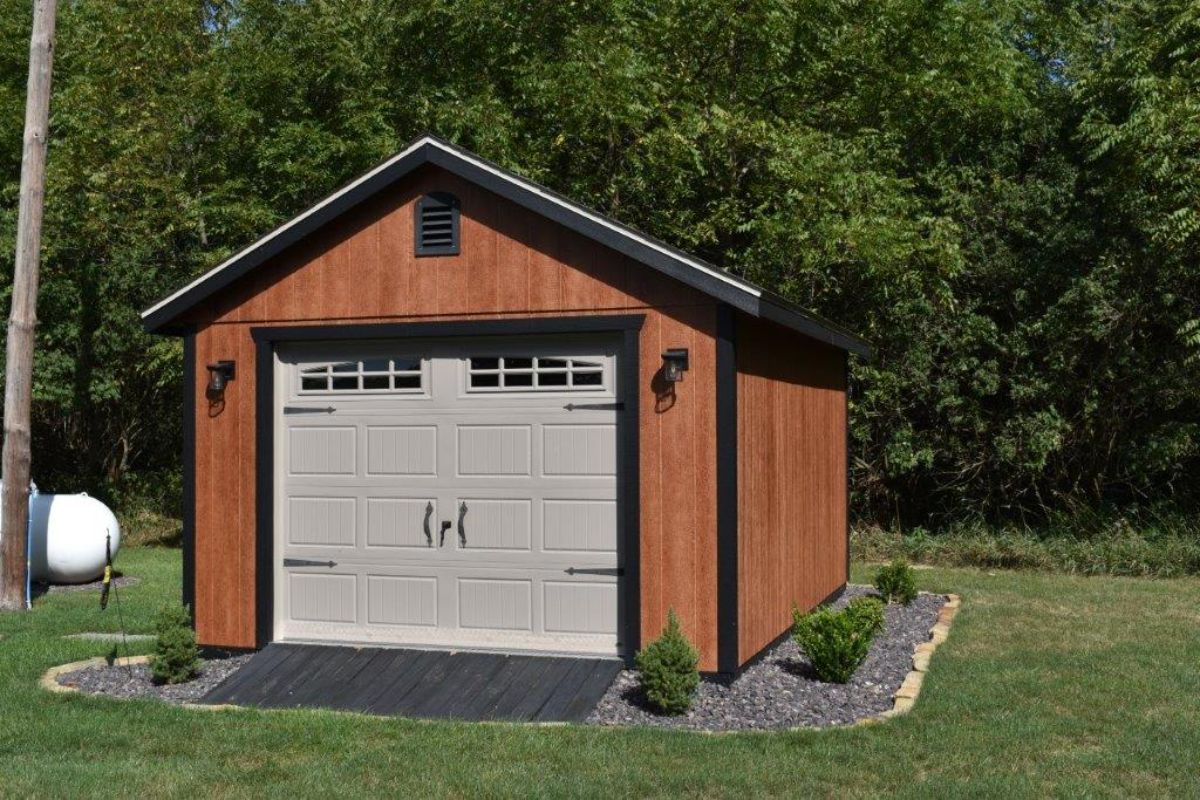 Wooden shed with gray garage door, brown siding, black trim, and landscaping.