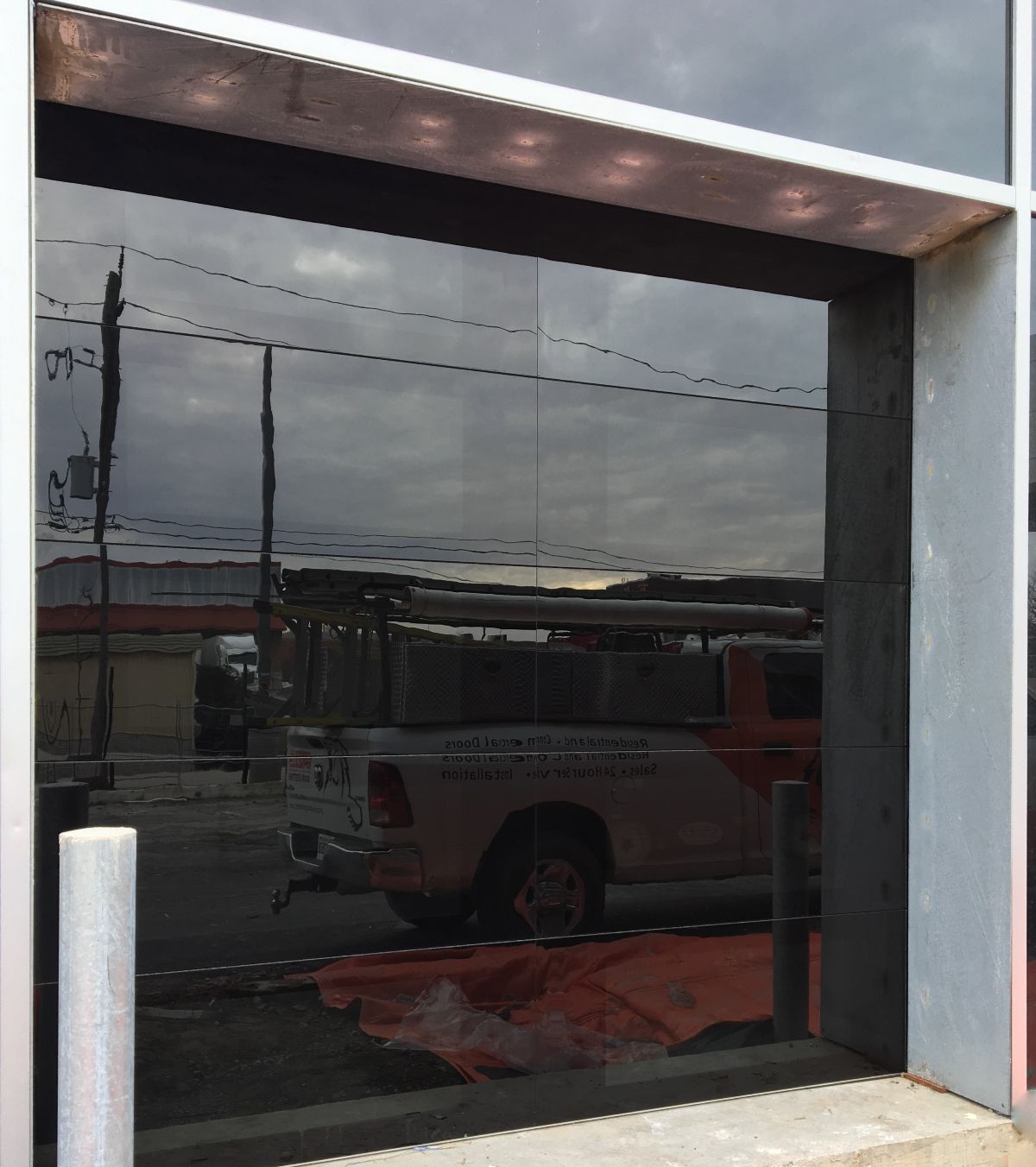 Exterior shot with dark reflective glass window; a truck, street, and cloudy sky reflected.