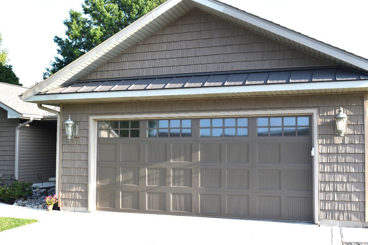 Brown garage door with window paneling, flanked by sconces, under a gabled roof.