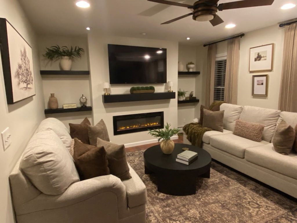 Living room with neutral tones: cream sofas, dark coffee table, fireplace, TV, and decorative shelves.