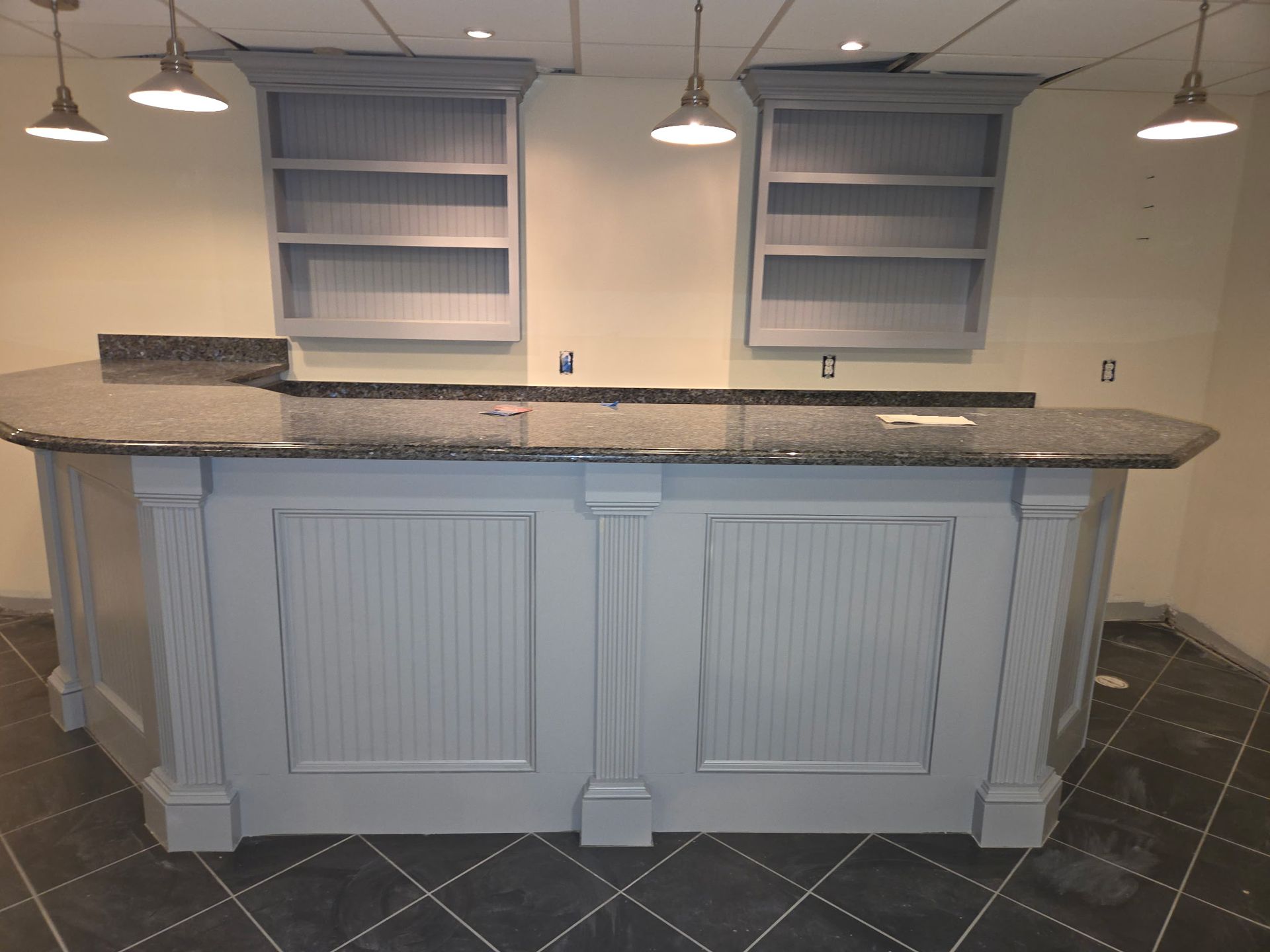 Gray bar with granite countertop, two shelves, pendant lights.