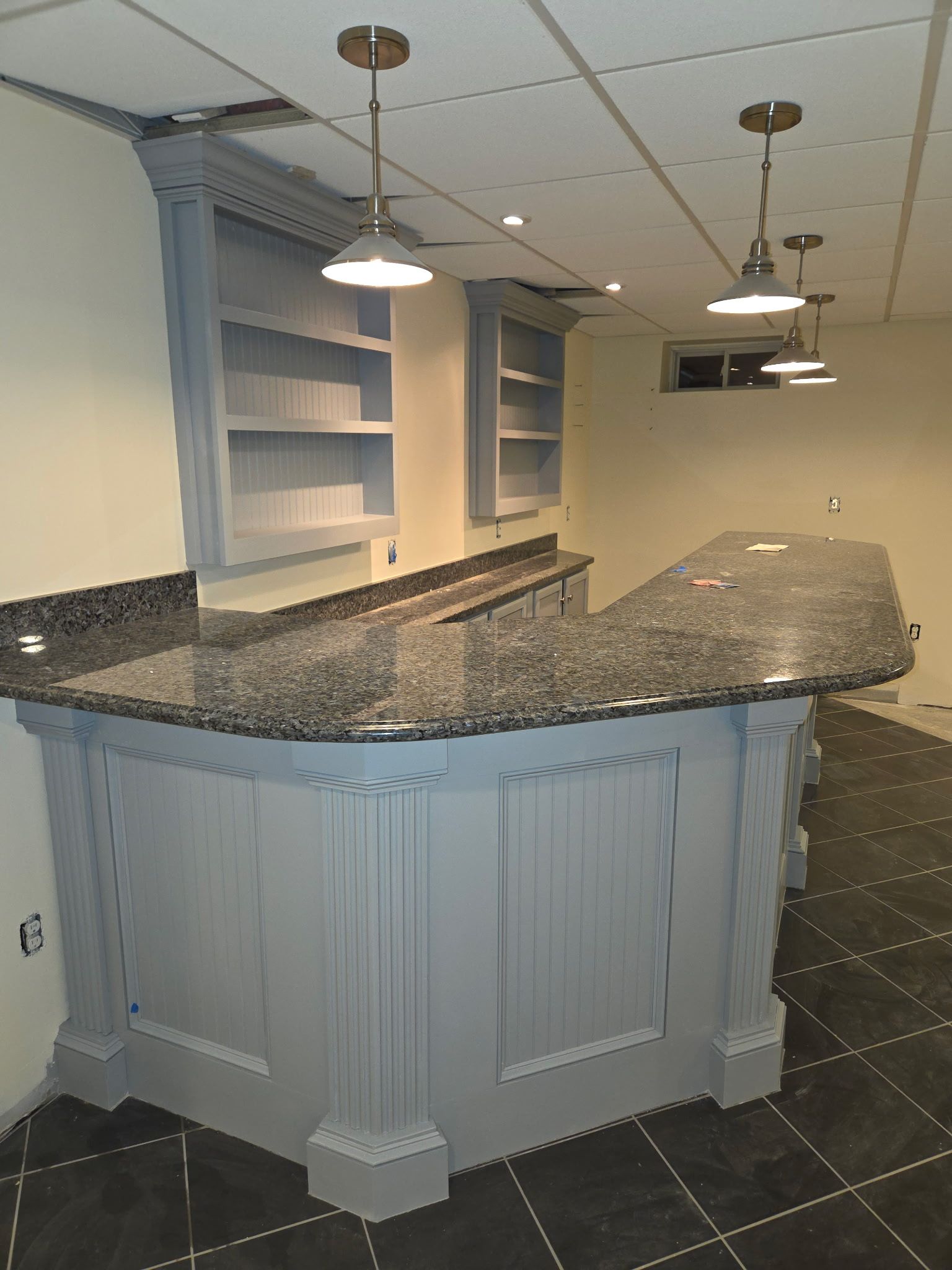 Gray bar with granite countertop, built-in shelving, and pendant lights in a basement setting.