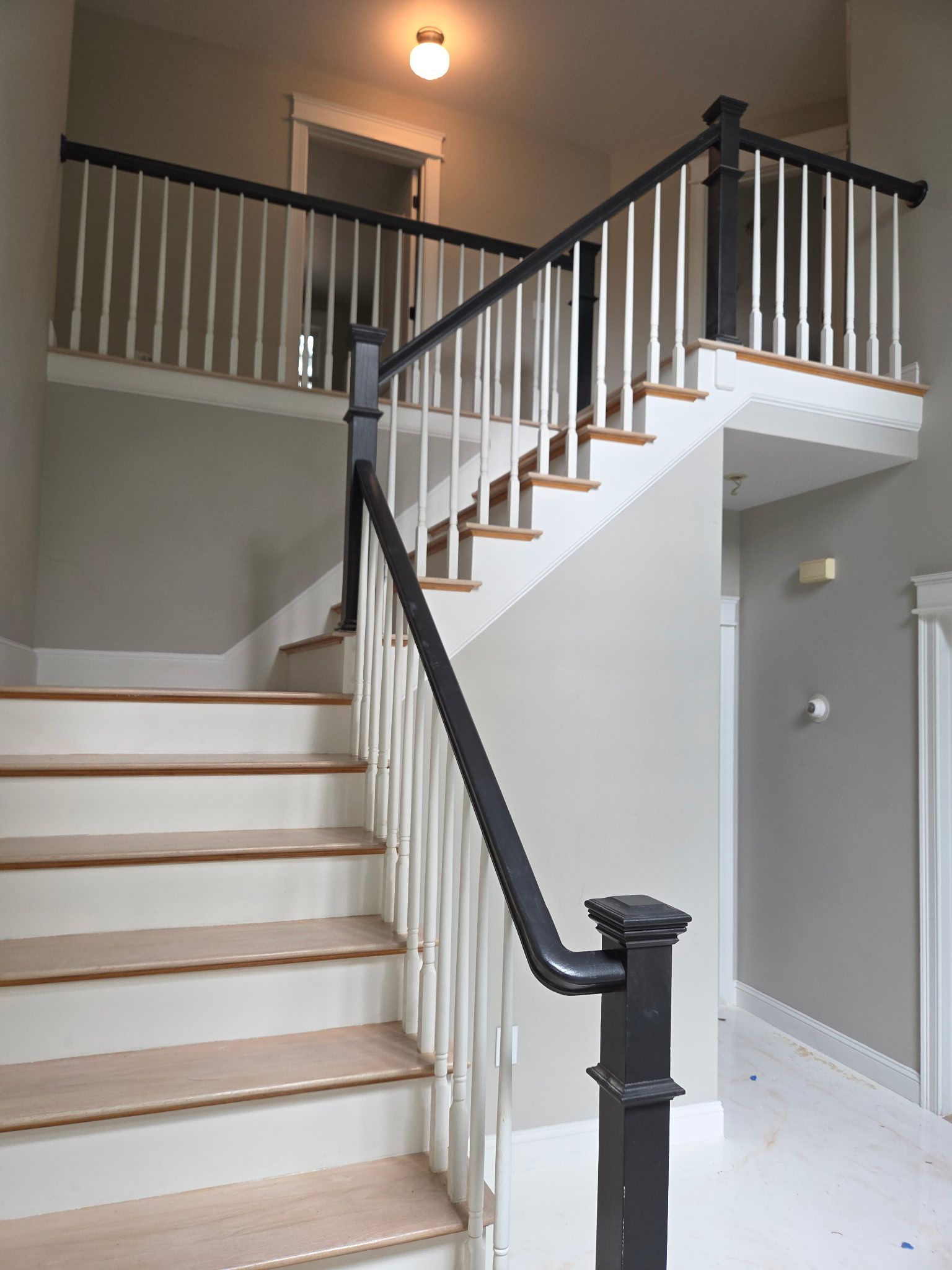 Staircase with white balusters and dark gray handrails and new wood steps.