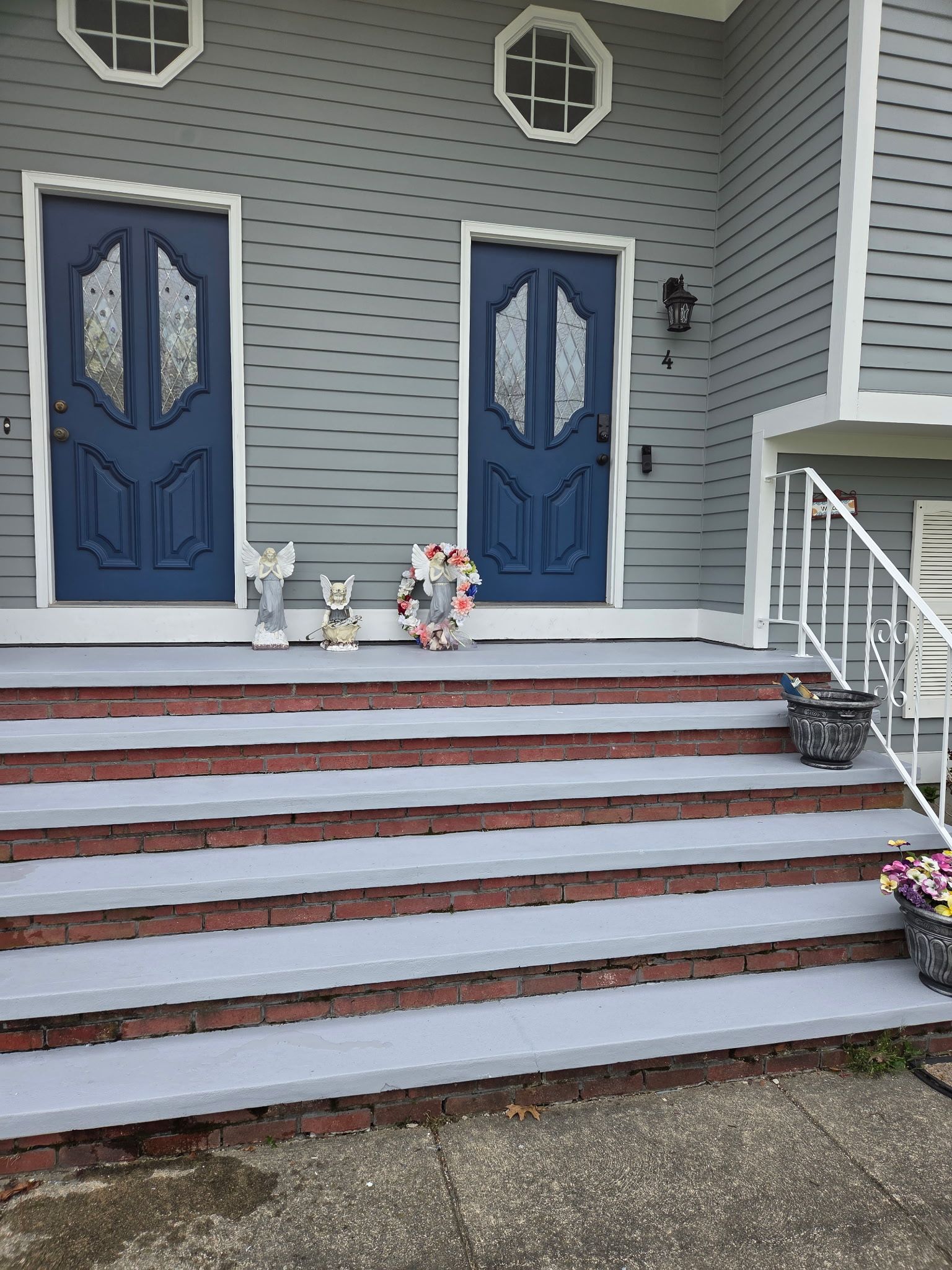 Two blue doors with decorative glass panels, leading to a gray house with steps. Statues and wreath.