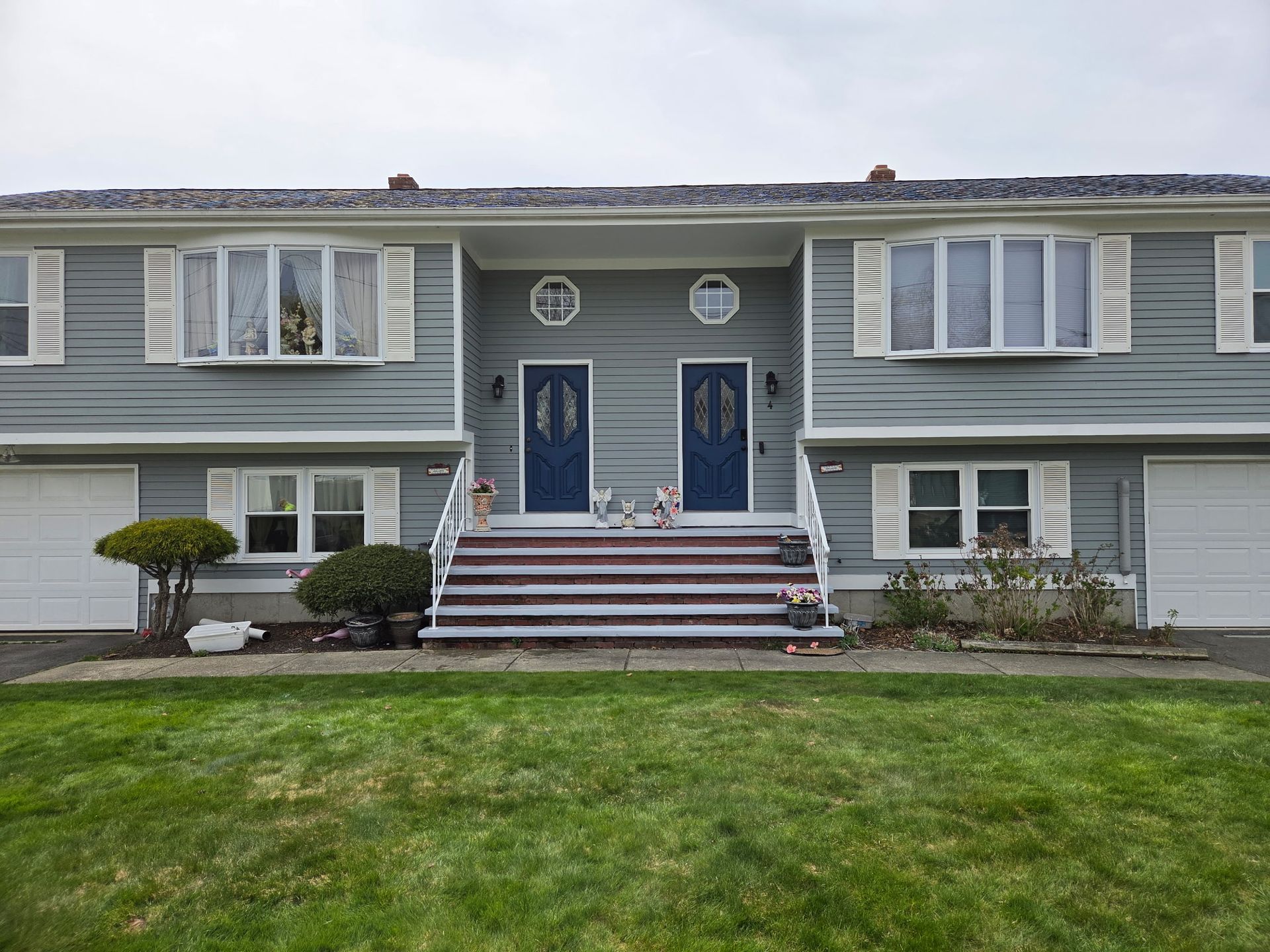 Two side-by-side gray houses with white trim, blue doors, and a green lawn in front.