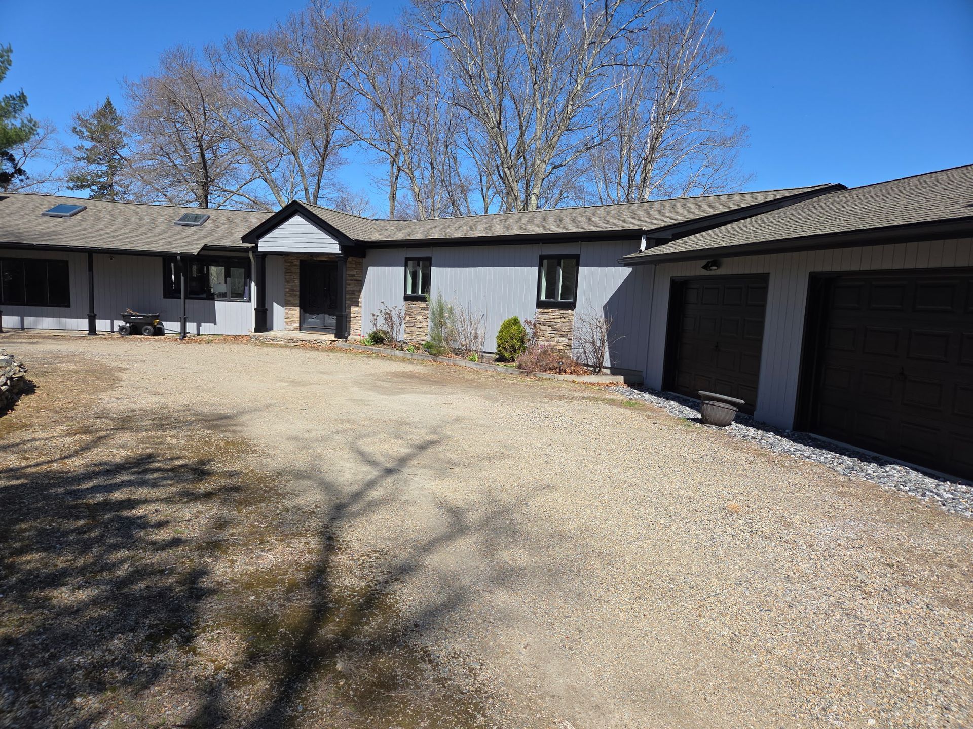 Gray ranch-style house with gravel driveway and two-car garage under a clear blue sky.